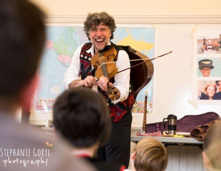 Image shows John Porcino smiling and playing a violin for an audience