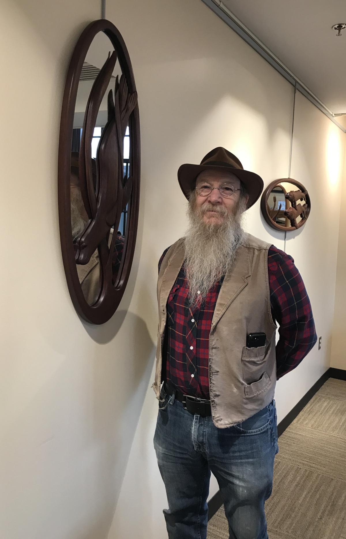 Man in a hat next to a wood carved mirror hanging